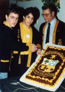 Three men in suits and ties cutting a cake.