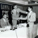 Two men shaking hands at a table with microphones.